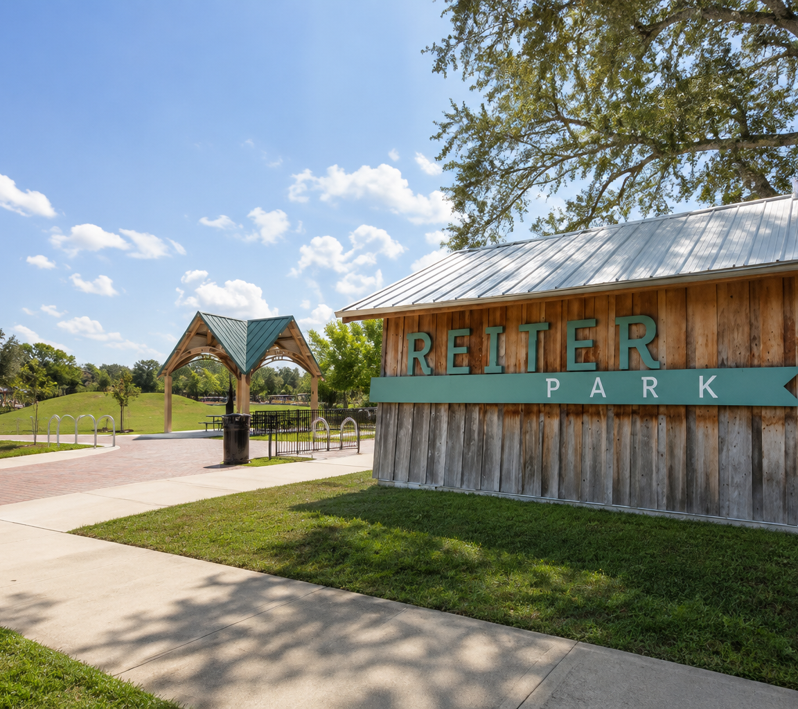 Timber park entrance structure with a metal roof beside a paved path and open lawn