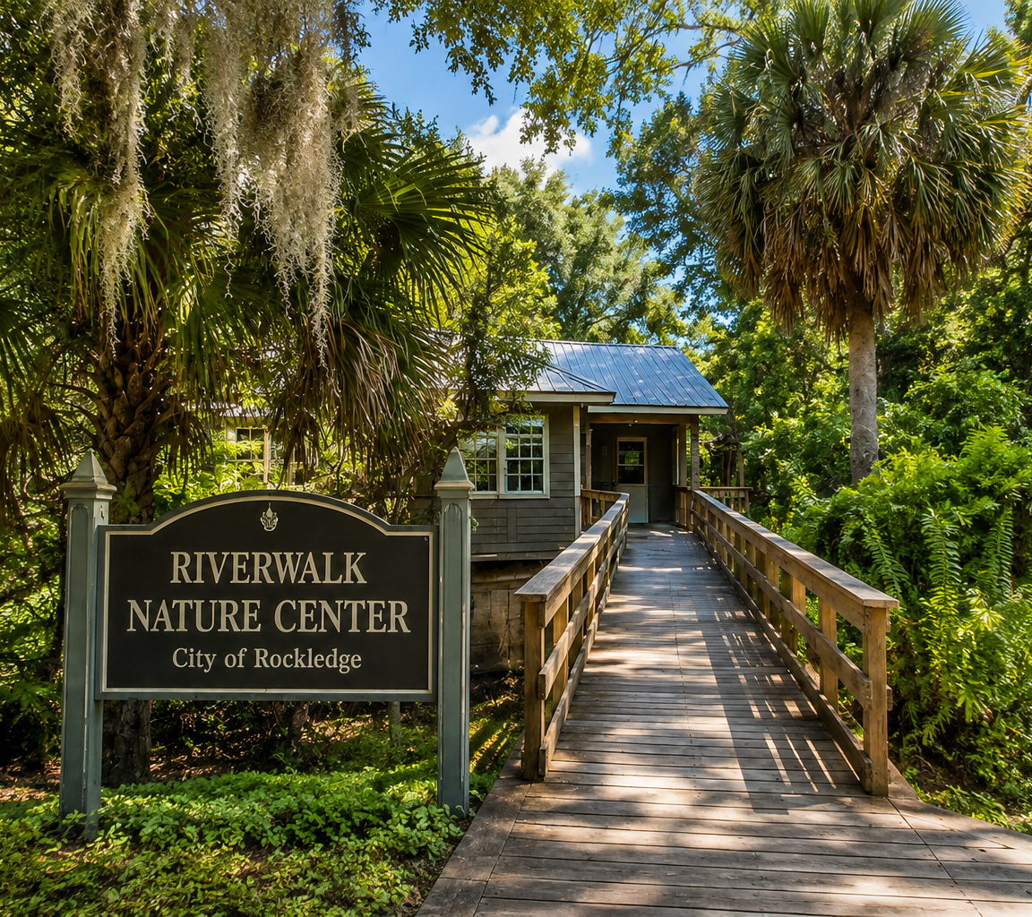Timber boardwalk leading to a small nature centre building, with a routed sign under palms and ferns