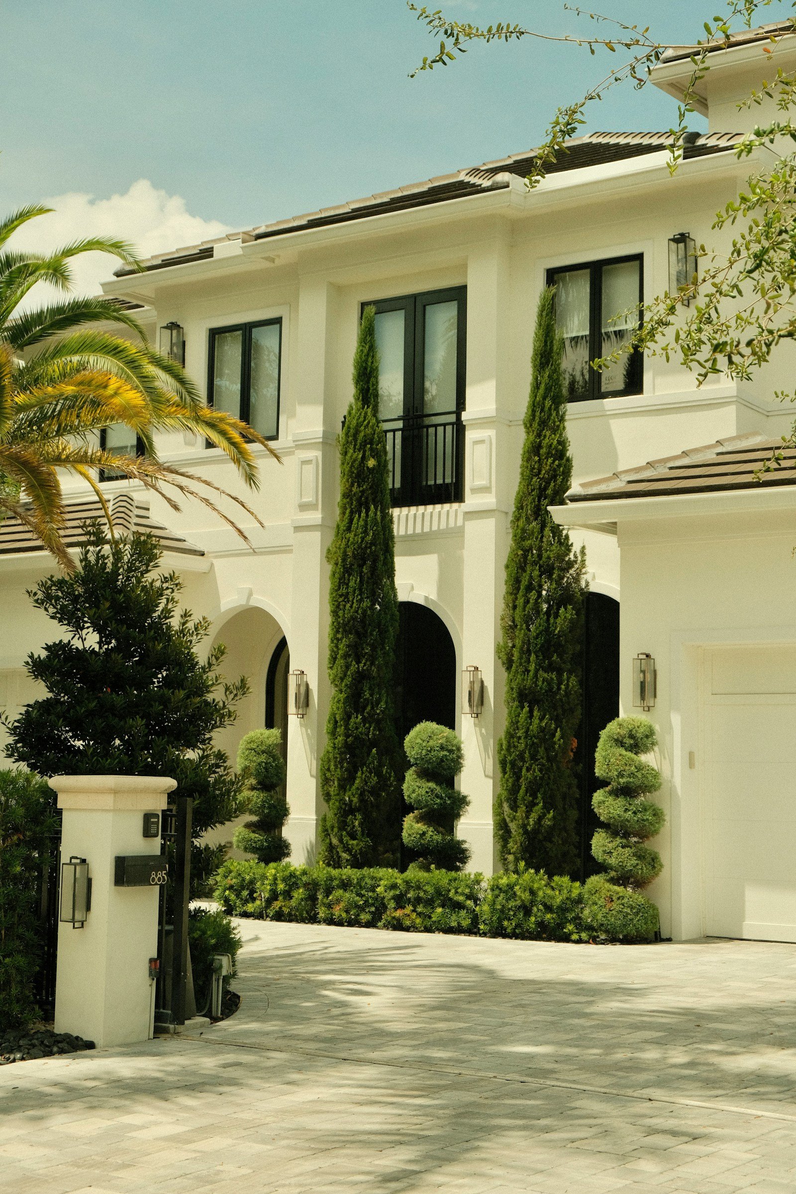 Large white house with manicured topiary and palms along a formal entry